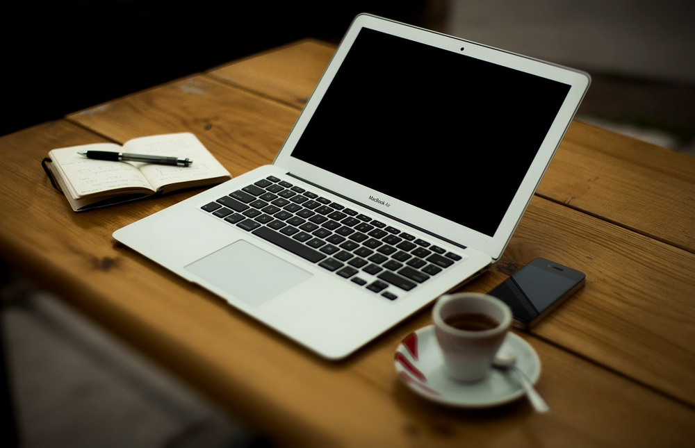 laptop with blank screen on wood table; coffee; pen and notepad