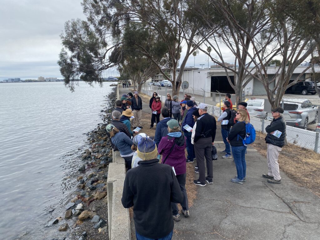 A group of people gathering on a paved walkway along the SF Bay
