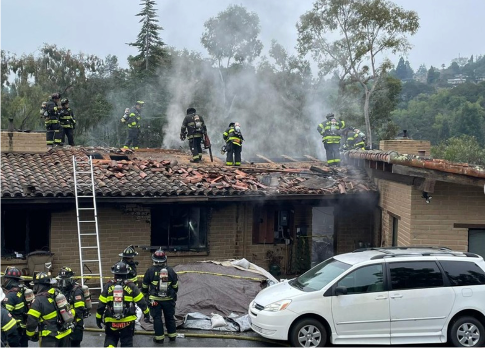 Multiple firefighters putting out a fire at a house with a damaged roof